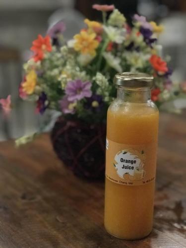 Una botella de jugo de naranja sobre una mesa con flores. en The Warehouse Chiang Mai, en Chiang Mai