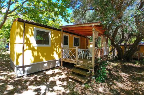 a yellow tiny house sitting under a tree at Mobile Homes Camp Perna - Adriatic Kampovi in Orebić