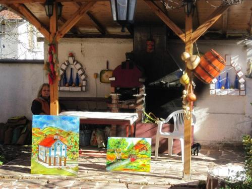 a woman sitting at a table with paintings on display at Hadjibulevata Guest House in Kovachevtsi