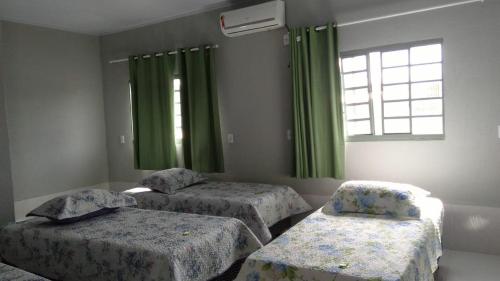 a bedroom with two beds and a window with green curtains at Pousada Agua Quente in Rio Quente