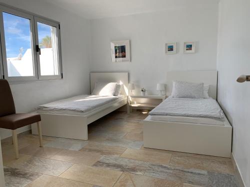 two beds in a room with a chair and a window at Villa Malagueñas in Puerto del Carmen