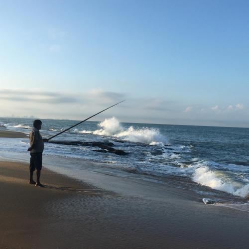 a man standing on the beach holding a fishing rod at Ayana Beach in Ja-Ela