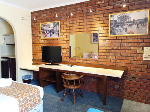 a room with a desk with a television on a brick wall at Glen Inn in Glen Waverley