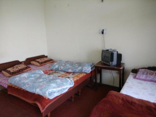 a room with two beds and a tv on a table at Shubham Home Stay in Kausani