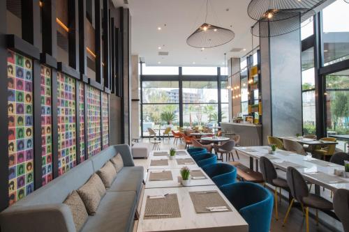 a restaurant with long tables and chairs and windows at ibis Styles Izmir Bornova in Izmir