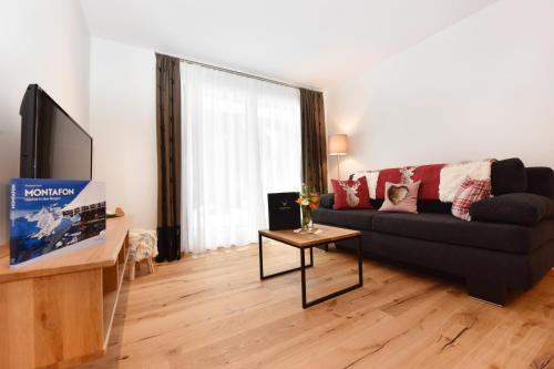 a living room with a black couch and a tv at Salzgeber Appartements in Sankt Gallenkirch