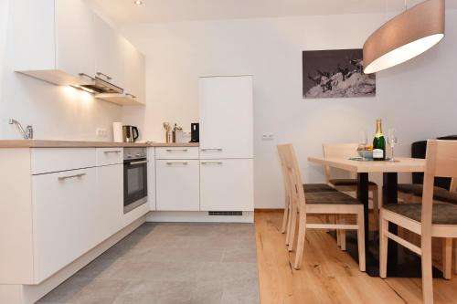 a kitchen with white cabinets and a table with chairs at Salzgeber Appartements in Sankt Gallenkirch