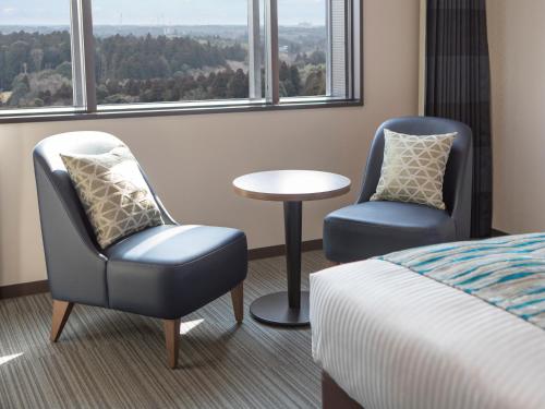 a room with two chairs and a bed and a table at HOTEL MYSTAYS PREMIER Narita in Narita