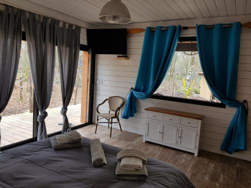 a bedroom with blue curtains and a bed and a chair at Au Bois Flotté in Hourtin