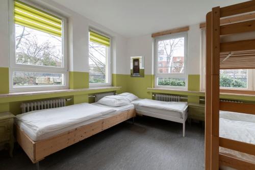 two beds in a room with three windows at Hostel Aachen in Aachen