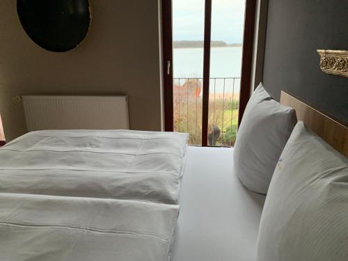 a bed with white sheets and pillows next to a window at Hotel Inselhof in Malchow