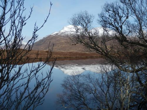 a snow covered mountain reflected in a lake with trees at 3 St Gilbert Street in Dornoch