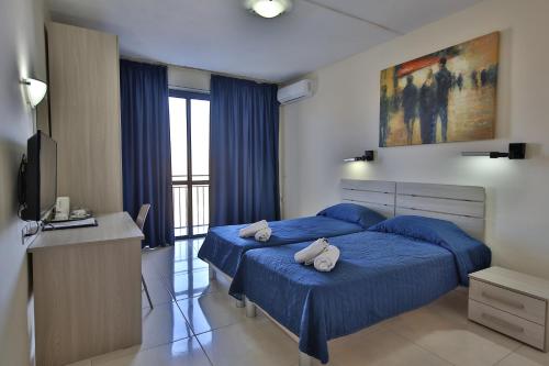 1 dormitorio con 2 camas azules y TV en Relax Inn Hotel, en St Paul's Bay