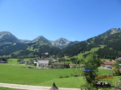 a village in a green field with mountains in the background at Haus Romantika in Schattwald