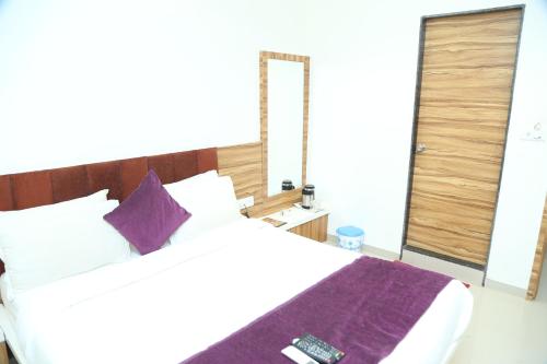 a bedroom with a white bed with a purple blanket at Shree Akshar Restaurant and Hotel in Ahmedabad