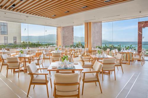 a dining room with tables and chairs and large windows at TMS Hotel Da Nang Beach in Da Nang