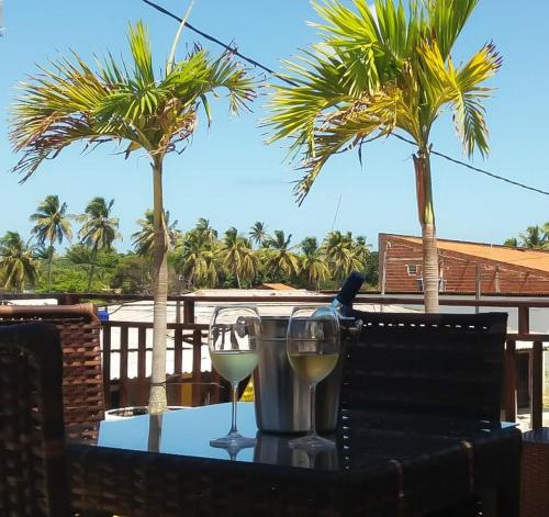 two glasses of white wine on a table with palm trees at Muriú Beach Flat in Muriú