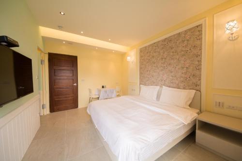 a bedroom with a large white bed and a flat screen tv at Yilan Siao Jhu in Jiaoxi