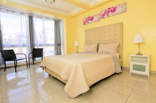 um quarto com uma cama grande, paredes amarelas e janelas. em RIG Puerto Malecón em Santo Domingo