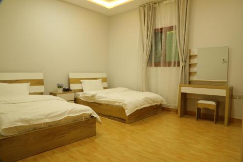 a bedroom with two beds and a desk and a mirror at Hala Onaizah in Unayzah