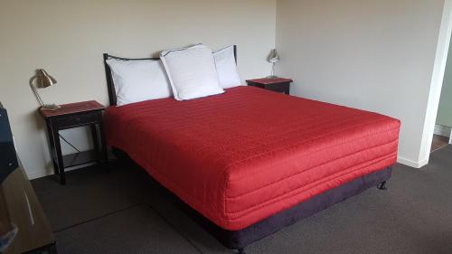 a bedroom with a red bed with two night stands at Palm Court Motel in Otorohanga