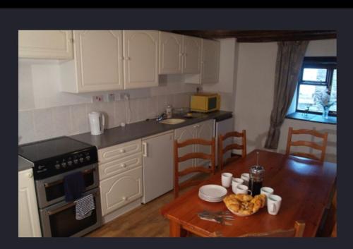 MertonにあるHayloft Cottageの白いキャビネット、木製テーブル(木製のテーブル付)が備わるキッチン