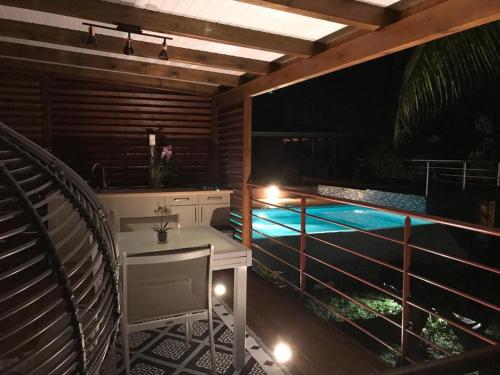 a balcony with a table and a swimming pool at night at Charmant bungalow au cœur de l’île in Baie-Mahault