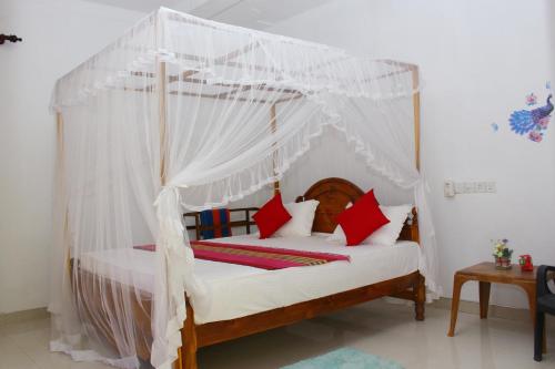 a bedroom with a canopy bed with red pillows at Pradeep Guest House in Mirissa