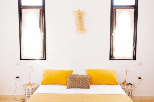a bedroom with a bed with yellow pillows and windows at La Maison des Ailleurs in Essaouira