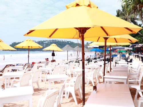 a beach area with umbrellas, chairs and tables at Fresh Wave Mirissa - Beach Front in Mirissa