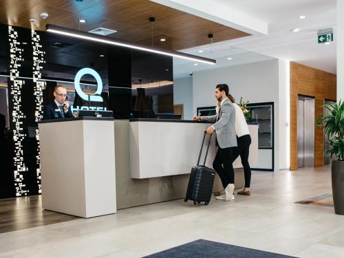 a woman with a suitcase waiting at a counter in an airport at Q Hotel Plus Katowice in Katowice