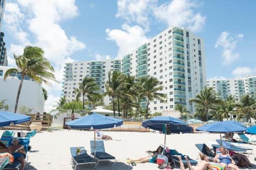 un groupe de personnes assises sur une plage avec des parasols bleus dans l'établissement The Tides on Miami Hollywood, à Hollywood