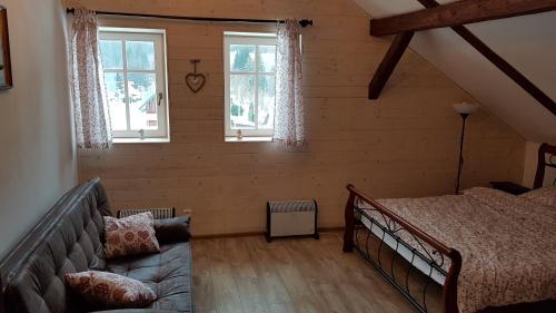 a bedroom with a bed and a couch and two windows at Chalupa 335 in Vítkovice