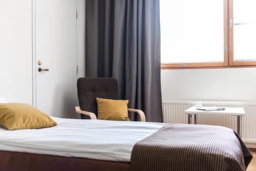 a bedroom with a bed and a chair and a window at Hotel Hermica in Tampere
