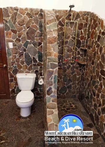 a bathroom with a toilet and a stone wall at White Chocolate Hills Resort in Zamboanguita