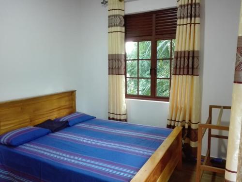 a bedroom with a bed with blue sheets and a window at Morris Bungalow in Passara