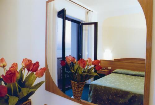 a mirror with a vase of flowers in a bedroom at Hotel Kennedy in SantʼAlessio Siculo