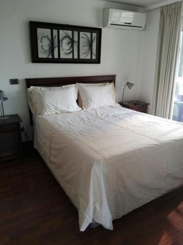 Una cama con sábanas blancas y almohadas en un dormitorio en Austral Rentahome Barros Borgoño, en Santiago