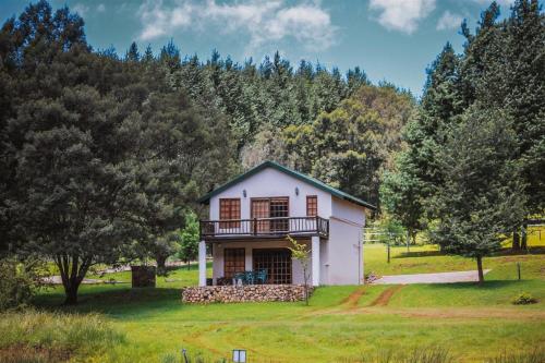 a small white house with a balcony in a field at Silver Mist Resort in Haenertsburg