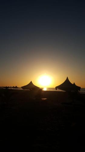 a sunset on a beach with tents and the ocean at Heather's Retreat in Brufut