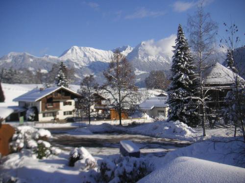 a house covered in snow with mountains in the background at Gästehaus Schmid in Obermaiselstein