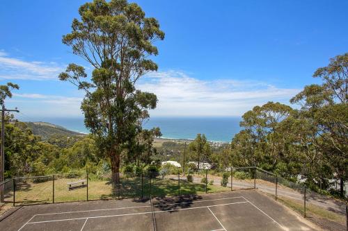 a tennis court with a tree and the ocean at Beacon Point Ocean View Villas in Apollo Bay