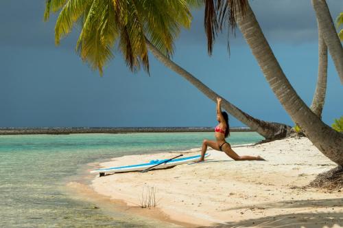 a woman is standing on a beach with a surfboard at Ninamu Resort in Tikehau
