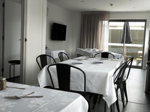 a dining room with white tables and chairs and a window at Stopforths Motel in Hokitika