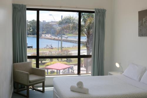 a bedroom with a bed and a chair and a large window at Aquarius Merimbula in Merimbula