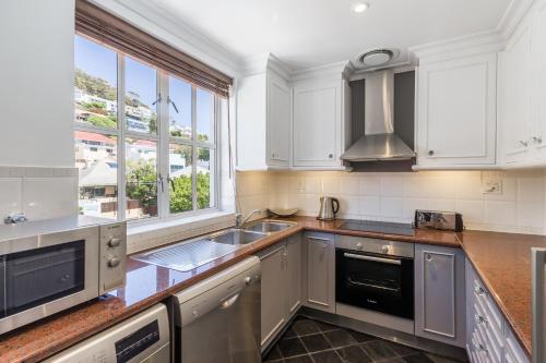 a kitchen with white cabinets and a sink and a window at Romney Park Luxury Apartments by The Stay Collection in Cape Town