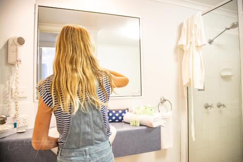 uma mulher a olhar para o seu reflexo num espelho de casa de banho em Mackay Seabreeze Apartments em Mackay