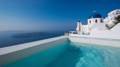 a swimming pool in front of a white building and a lighthouse at Alexander Villas in Imerovigli
