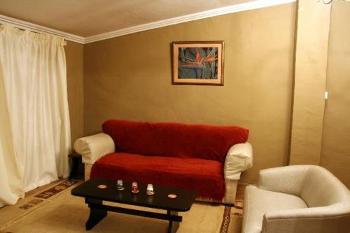 a living room with a red couch and a table at Rugare Sweet Dreams Holiday Cottage in Curryʼs Post
