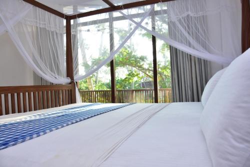 a bedroom with a bed with white sheets and a window at Green Almond Hotel in Unawatuna